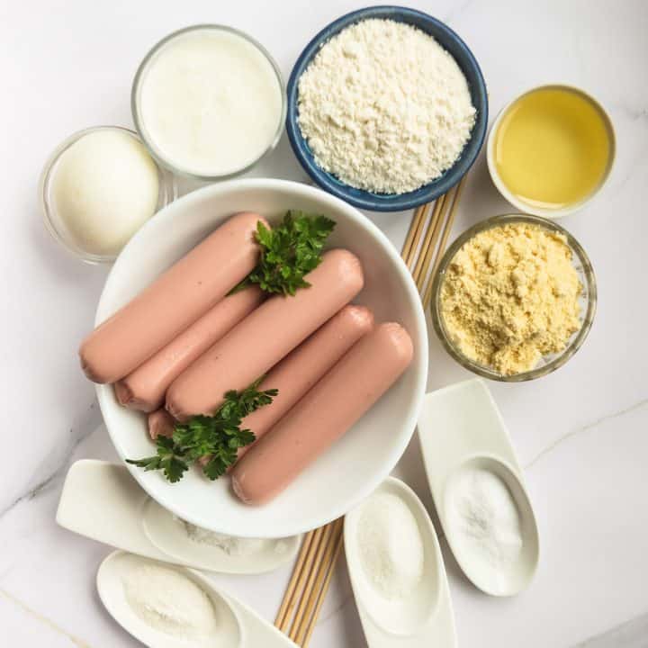 Plate of hot dogs on skewer surrounded by dry ingredient to make corn dogs.