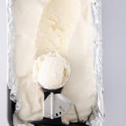 Ice cream scoop of vanilla ice cream on top of loaf pan filled with homemade ice cream.