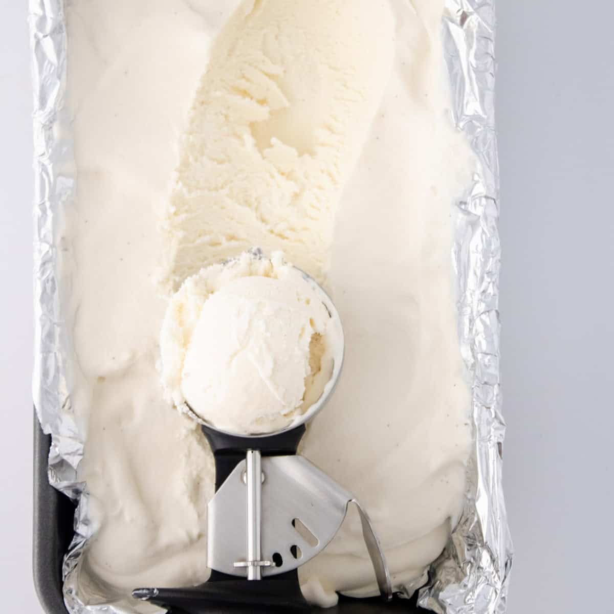 Ice cream scoop of vanilla ice cream on top of loaf pan filled with homemade ice cream.
