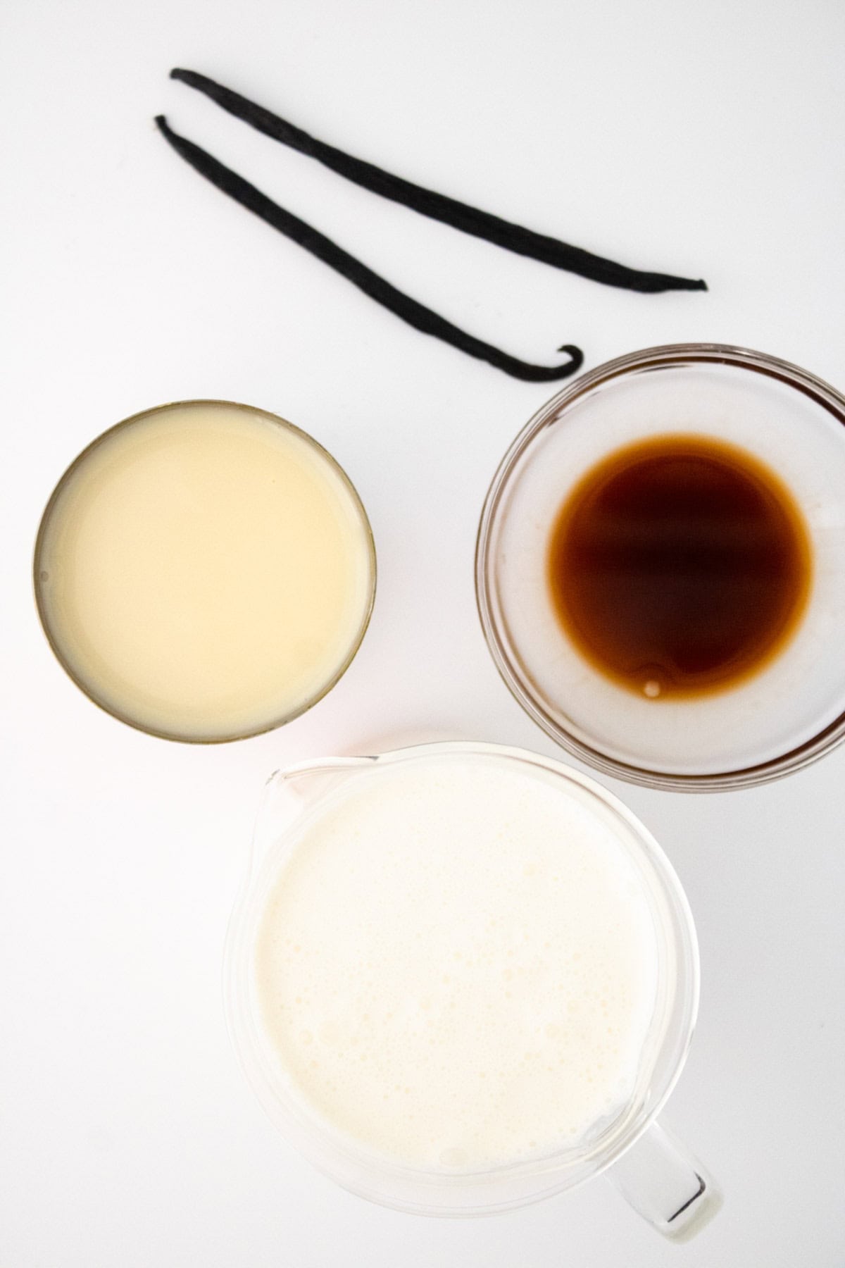 Vanilla, vanilla bean, heavy cream and sweetened condensed milk measured out  in bowls.