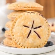 A close-up of stacked round blueberry pie cookies with a golden crust and star-shaped slits on top, revealing a blueberry filling inside.