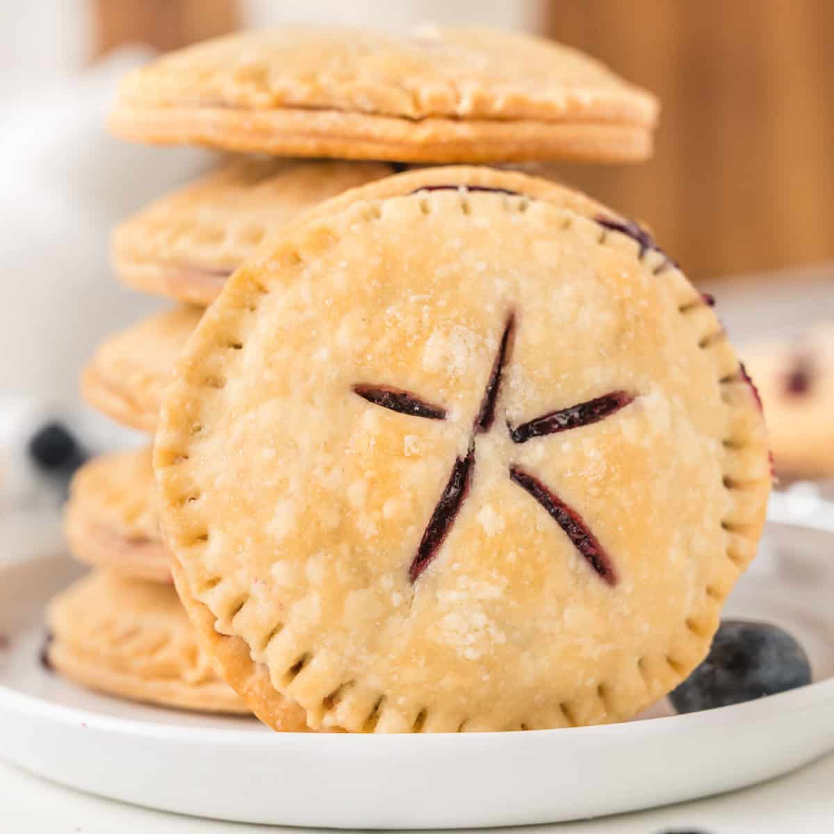A close-up of stacked round blueberry pie cookies with a golden crust and star-shaped slits on top, revealing a blueberry filling inside.