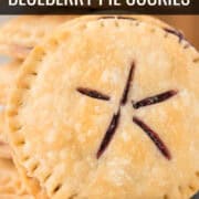 Close-up of round blueberry pie cookies with crimped edges and star-shaped slits in the center, stacked on a white plate. Close-up of round blueberry pie cookies with crimped edges and star-shaped slits in the center, stacked on a white plate.