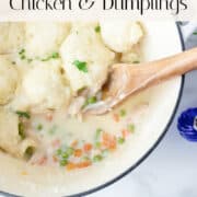 White Dutch oven filled with chicken and dumplings and a wooden spoon on a marble countertop, garnished with fresh parsley; lid placed to the side.