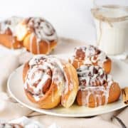 A plate of cinnamon rolls drizzled with icing, with more rolls and a glass of milk in the background.