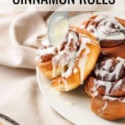 Cinnamon rolls drizzled in cream cheese icing on white plate.