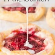 A spoon drizzles white icing over a raspberry danish pastry on parchment paper, with other pastries visible in the background.