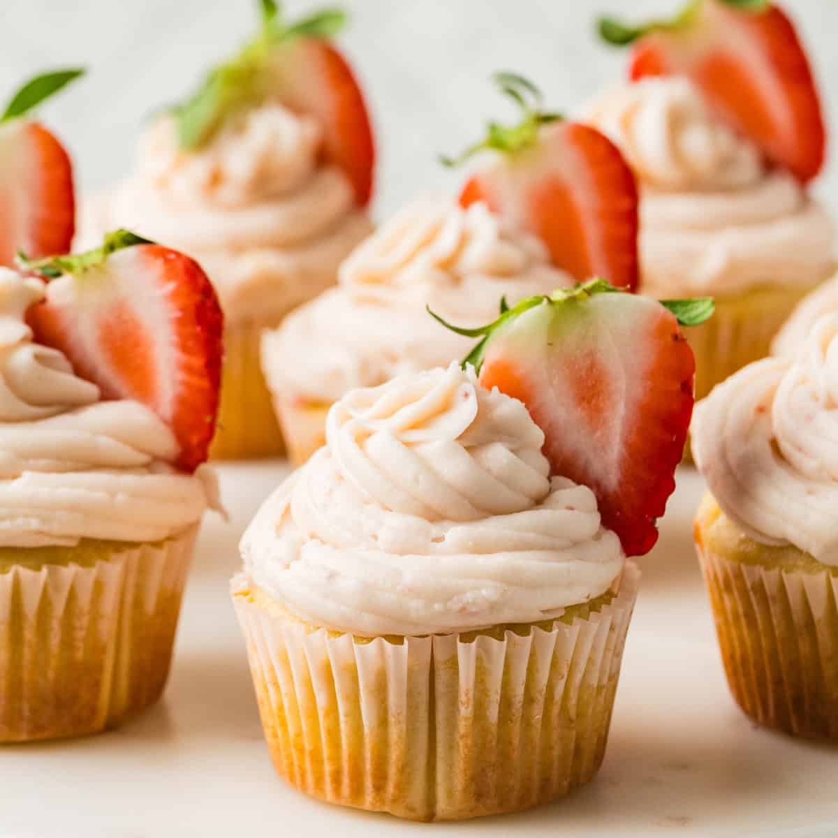 Cupcakes topped with swirled frosting and garnished with fresh strawberry halves on a white surface.