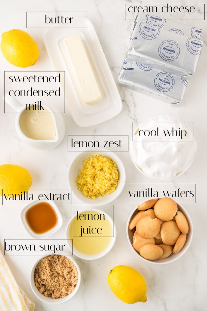 Ingredients for a no bake lemon cheesecake recipe displayed on a white surface: butter, cream cheese, sweetened condensed milk, cool whip, vanilla wafers, brown sugar, lemon juice, lemon zest, and vanilla extract.