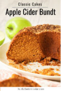A close-up of a sliced apple cider bundt cake with a golden brown crust on a white plate. Fresh green apples are in the background, and crumb topping is scattered around the cake.