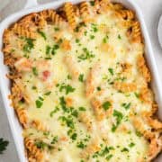 A baked casserole dish filled with rotini pasta, chicken, tomato sauce, and melted cheese, topped with chopped parsley.