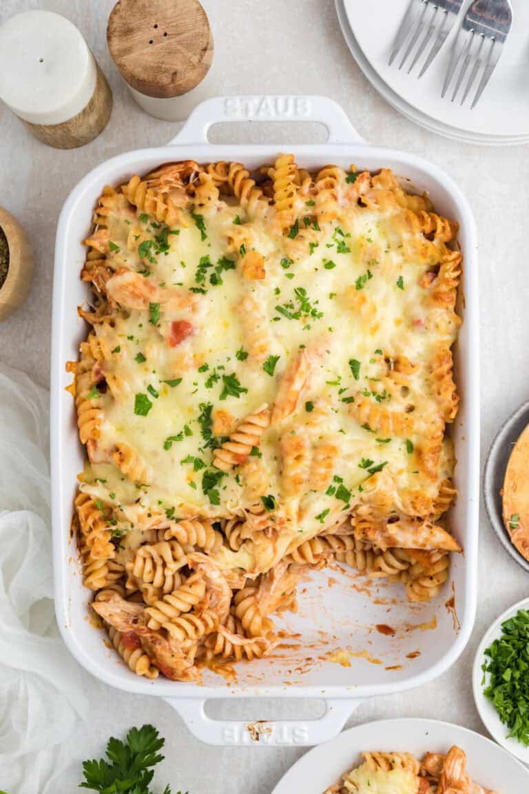 Baked rotini pasta with melted cheese and tomato sauce, garnished with chopped parsley, served in a white ceramic dish.
