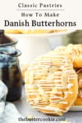 A close-up of Danish butterhorn pastries topped with white icing and sliced almonds, with a blue jug and a blue-checked napkin nearby. Text reads: How to Make Danish Butterhorns and thebuttercookie.com.