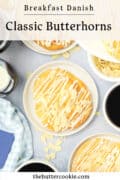 Overhead view of plates with round danish butterhorn pastries drizzled with white icing and topped with almond slices, next to coffee, syrup, and a bowl of sliced almonds. Text reads: Classic Butterhorns, thebuttercookie.com.