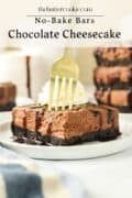 A fork cutting into a slice of no-bake chocolate cheesecake bar with an Oreo crust, drizzled with chocolate, served on a white plate with whipped cream in the background.