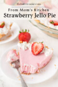 A slice of strawberry jello pie topped with whipped cream and a halved strawberry sits on a white plate with a fork. The whole pie is in the background, along with another plate of pie. Text reads: From Mom’s Kitchen Strawberry Jello Pie.