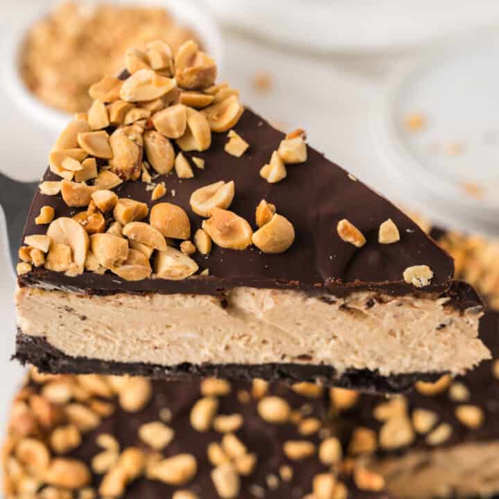 A slice of chocolate peanut butter cheesecake topped with chopped peanuts, featuring a creamy peanut butter layer, a chocolate topping, and an Oreo cookie crust.