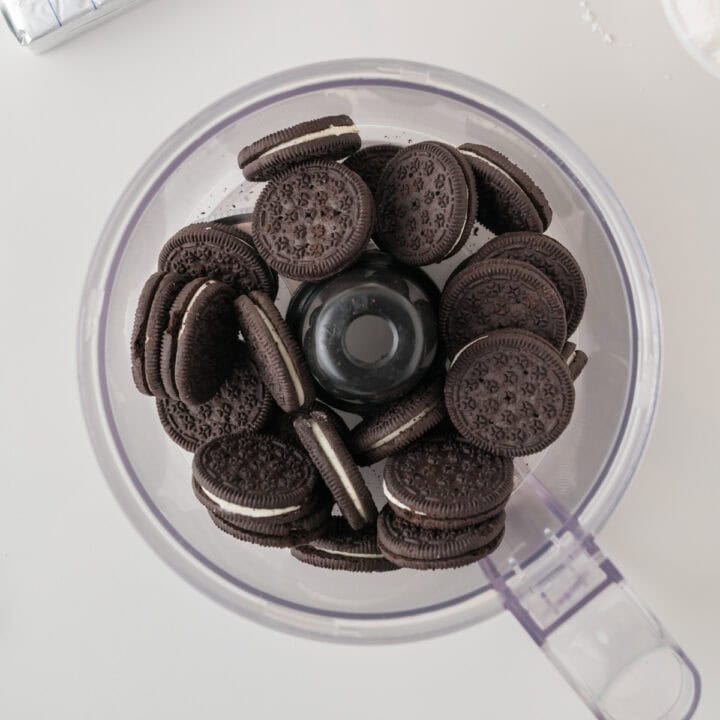 A food processor bowl filled with whole chocolate sandwich cookies, viewed from above on a white surface.