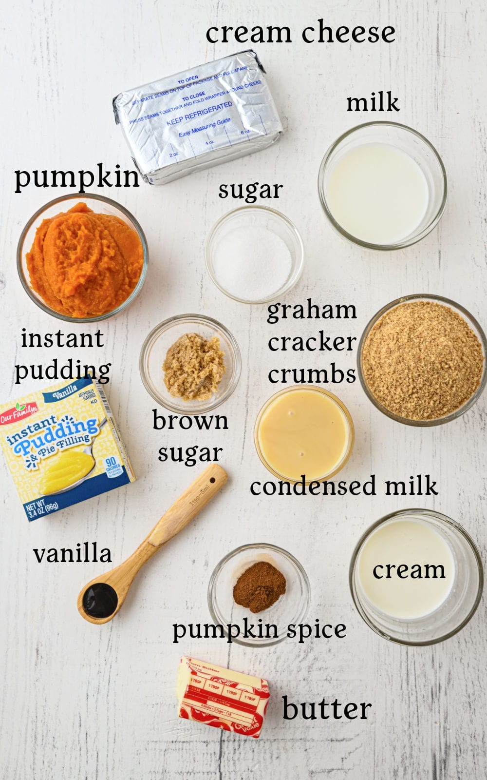 Top view of ingredients for a pumpkin dessert on a white surface, labeled: cream cheese, milk, sugar, pumpkin, instant pudding, brown sugar, graham cracker crumbs, condensed milk, cream, pumpkin spice, vanilla, and butter.