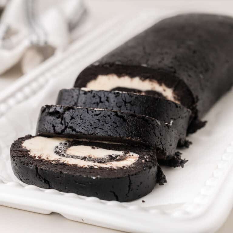 A chocolate oreo cake roll with a white cream filling is sliced and arranged on a white rectangular platter. The roll has a dark, rich appearance and a visible spiral pattern in each slice.
