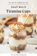 A small glass jar filled with layers of tiramisu, topped with whipped cream and cocoa powder, with a gold spoon. The text above reads Small Batch Tiramisu Cups and below is by aweekendcook.com.