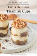 A close-up of tiramisu served in small glass jars, topped with whipped cream and cocoa powder, set on a white plate. Text reads: Easy & Delicious Tiramisu Cups by aweekendcook.com.